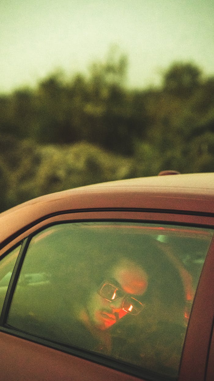A man wearing sunglasses inside a car at twilight with a reflective atmosphere.