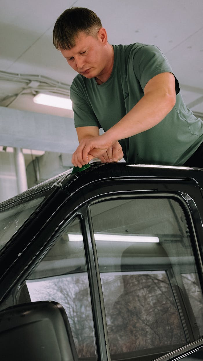 Adult man applying window tint on car indoors.