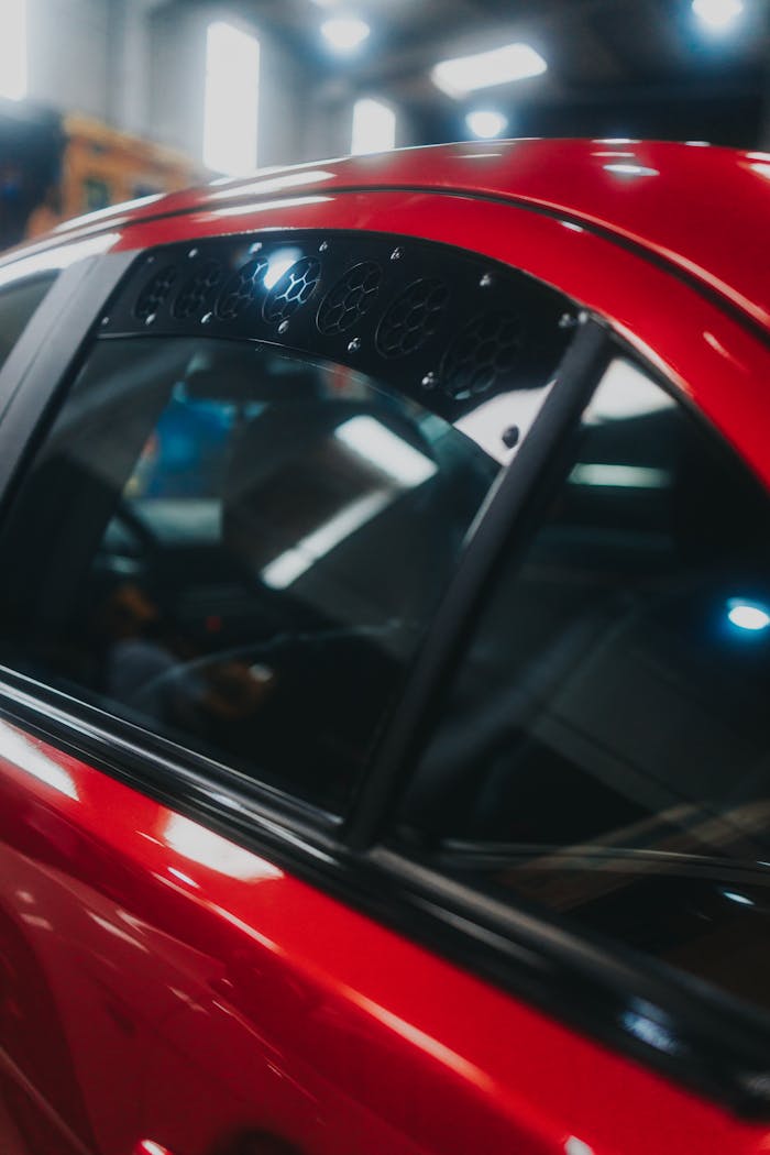 A focused shot of a red cars side window reflecting indoor lights.